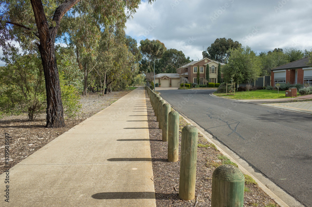 Pedestrian walkway in a quiet residential neighbourhood with some suburban houses in the distance. Concrete footpath in an Australian suburb with Eucalyptus trees long the road.  Copy space for text.