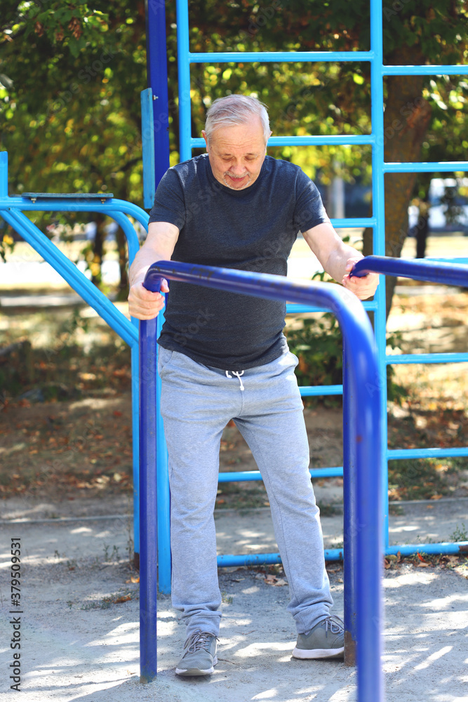 Fototapeta premium Senior man doing exercises in the outdoor gym. The concept of maintaining health at any age. Recovering from a heart attack or stroke. Selective focus. Toning.