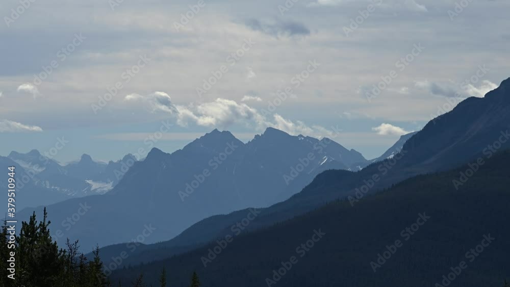 Time lapse of white and grey clouds developing in a grey cloudy morning sky above large mountain. The mountains in many shades of blue, a forest is in the foreground and glaciers on the mountains.
Time lapse of white and grey clouds developing in a grey cloudy morning sky above large mountain. The mountains in many shades of blue, a forest is in the foreground and glaciers on the mountains.