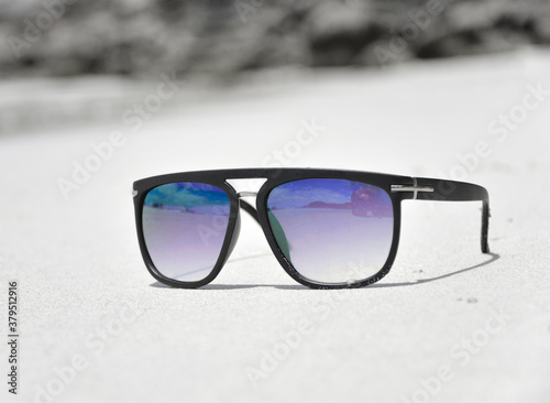 Dark sunglasses on the sand with black frames.