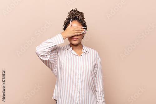 young afro woman covering eyes with one hand feeling scared or anxious, wondering or blindly waiting for a surprise photo