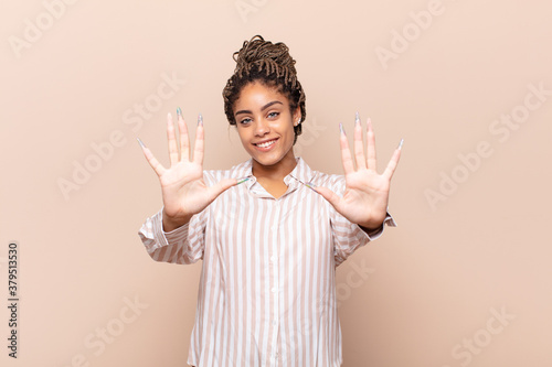 young afro woman smiling and looking friendly, showing number ten or tenth with hand forward, counting down