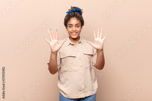 young afro woman smiling and looking friendly, showing number ten or tenth with hand forward, counting down photo