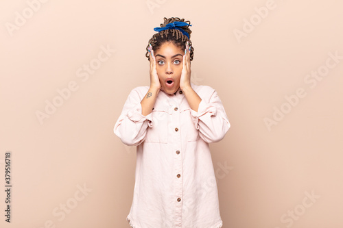 young afro woman looking unpleasantly shocked, scared or worried, mouth wide open and covering both ears with hands photo