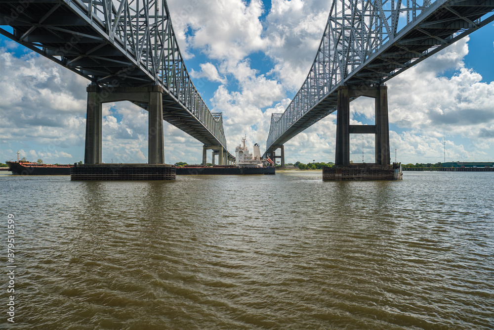 Interstate 10 Twin Span bridge over the Mississippi River in New Orleans, Louisiana with a cargo ship cruising by. Interstate 10 Twin Span bridge over the Mississippi River in New Orleans, Louisiana with a cargo ship cruising by.