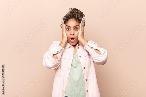 young afro woman looking unpleasantly shocked, scared or worried, mouth wide open and covering both ears with hands photo