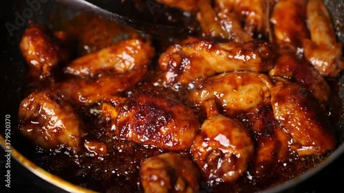 Slow motion closeup of hot chicken wings being cooked on a non stick pan steaming hot