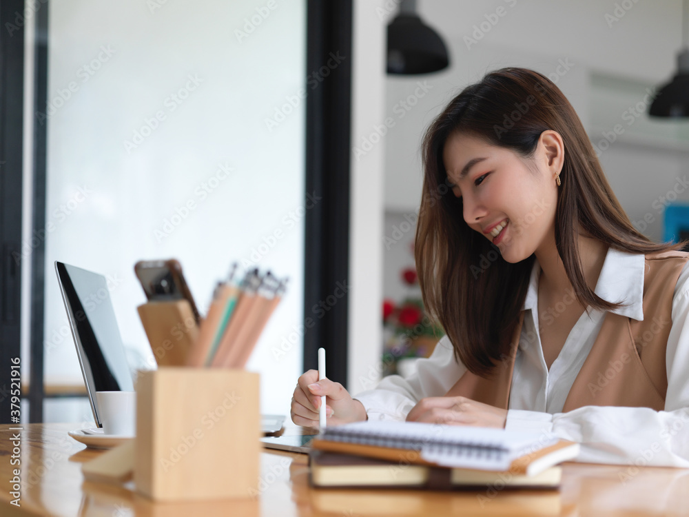 Portrait of smiling female university student doing assignment with digital devices and stationery
