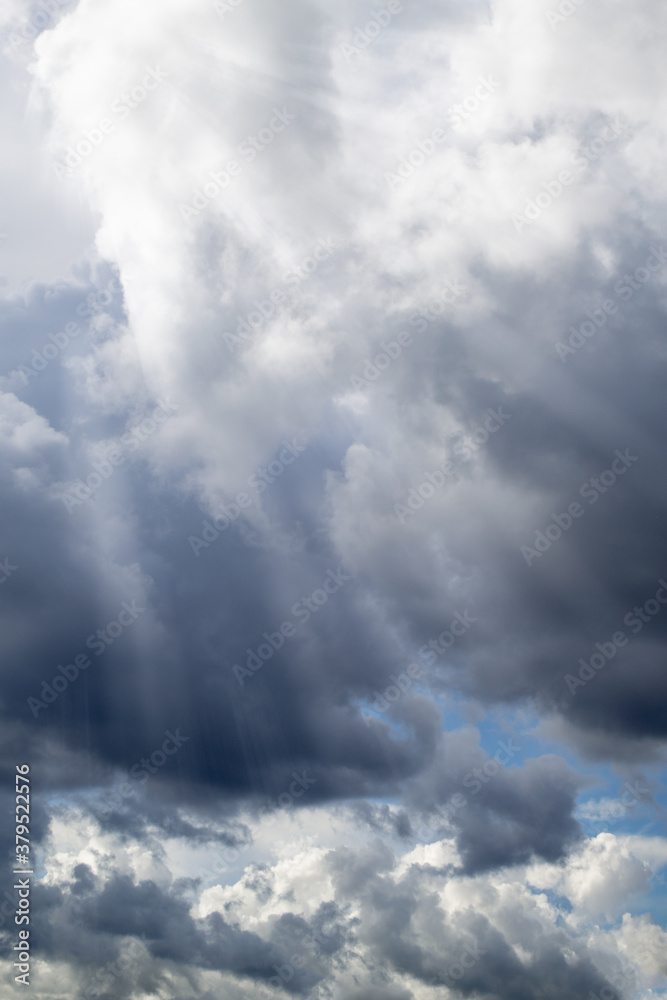 Dramatic clouds. Bright sunlight shines through the rain clouds. Autumn - spring weather. Vertical photo