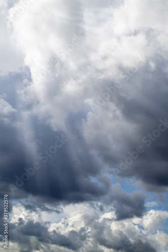 Dramatic clouds. Bright sunlight shines through the rain clouds. Autumn - spring weather. Vertical photo