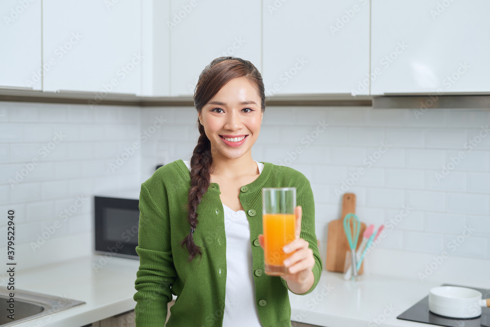 Portrait of a smiling young woman drinking orange juice in the kitchen at home Portrait of a smiling young woman drinking orange juice in the kitchen at home