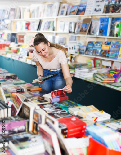 Portrait of positive young woman choosing textbooks in book shop..