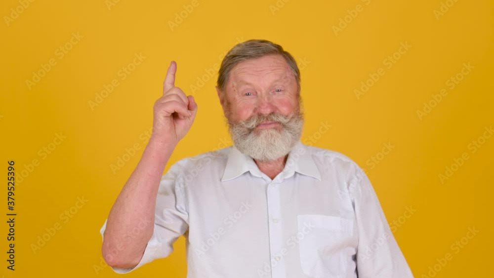 Portrait of an Elderly Gray-haired Man with a Beard Meditates and Raises His Thumb Up against a Studio Yellow Background. Thinking man looking looking at the camera Portrait of an Elderly Gray-haired Man with a Beard Meditates and Raises His Thumb Up against a Studio Yellow Background. Thinking man looking looking at the camera