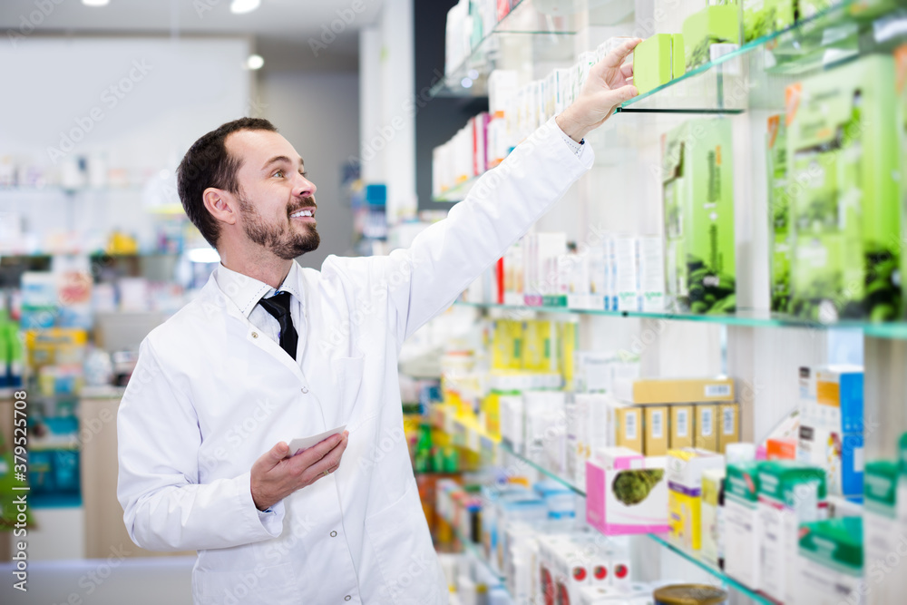 Smiling man pharmacist looking rows of drugs in drustore