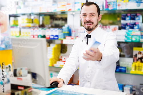 Smiling young man pharmacist writing down assortment of drugs in pharmacy