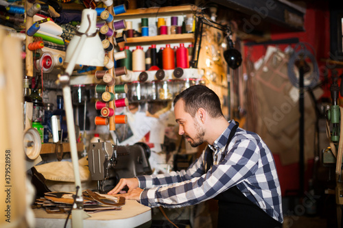 Positive adult male stitching new belt in leather workshop