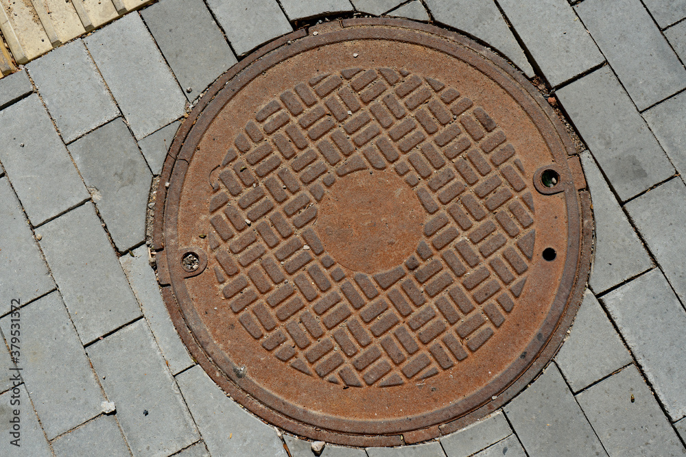 Round iron rusty sewer manhole on the city sidewalk.