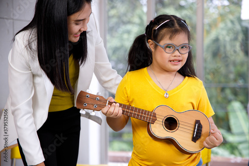 Asian teacher teach ukulele to girl with Down's syndrome.