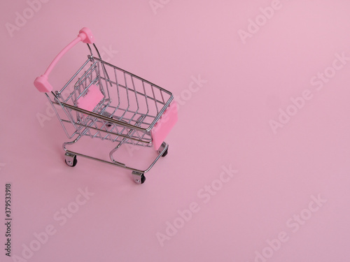 Small shopping cart with big cucumber on pink background