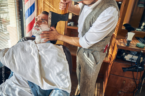 Hairdresser operating an axe while shaving his customer