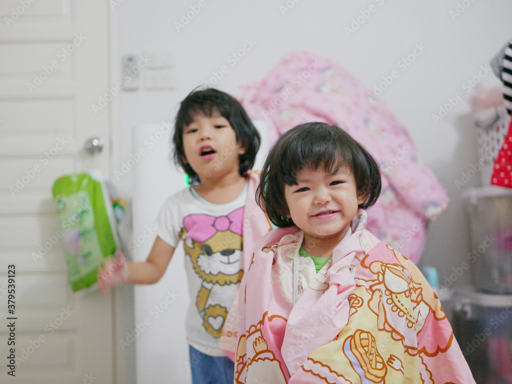 Little baby girl, 2 years old, ( right ) enjoys playing at home by covering herself with a bedsheet - allowing children to use their creativity by playing with anything around them Little baby girl, 2 years old, ( right ) enjoys playing at home by covering herself with a bedsheet - allowing children to use their creativity by playing with anything around them