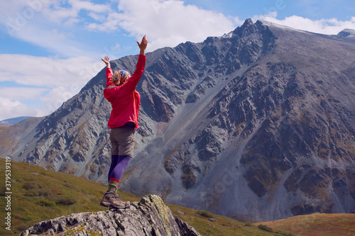 The girl in the red jacket happily raised her hands up. The girl travels in the mountains.
