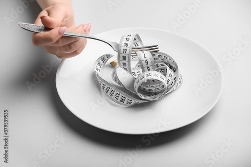 Female hand with plate, fork and measuring tape on grey background. Concept of anorexia photo