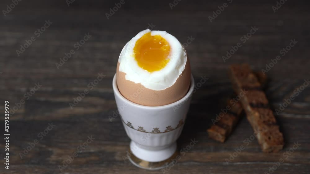 Soft boiled brown egg and toast bread in eggcup on wooden table background. Close up. Healthy breakfast