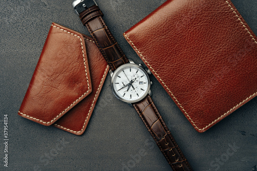 Male watch and leather wallet on dark grey surface