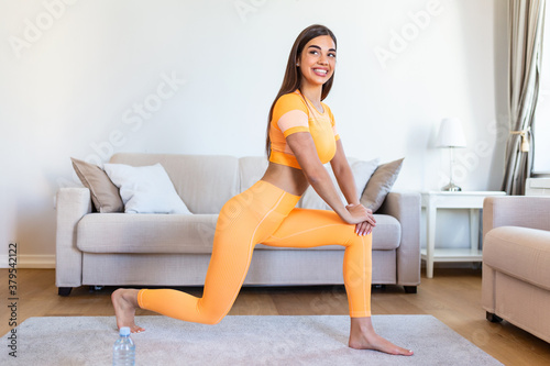 Young woman exercising at home, stretching. Time for yoga. Attractive and healthy young woman doing exercises while resting at home. Young woman exercising on carpet at home, interior