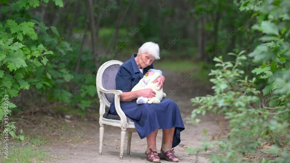 Grandmother holding baby infant sitting on a chair in a beautiful park. Grand parent bonding with grand-child Grandmother holding baby infant sitting on a chair in a beautiful park. Grand parent bonding with grand-child