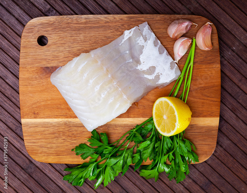 Fresh raw kingklip fillet with greens, lemon and spices on wooden background. Cooking ingredients photo