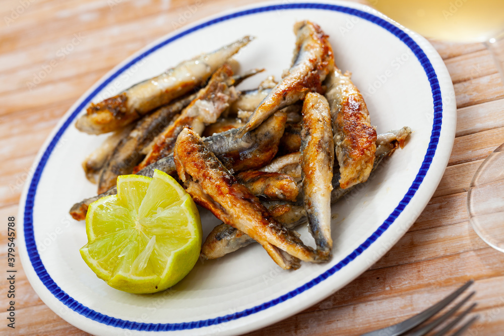 Tasty fried anchovies served with lemon at plate, Spanish cuisine