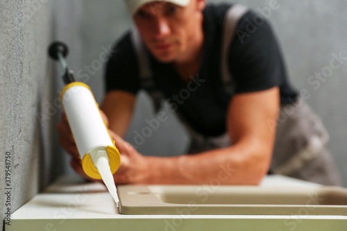 worker seals kitchen sink with sealant. hands of worker works with construction sealant gun in the kitchen. 