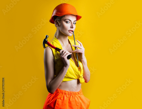 Sexy woman in helmet to use hammer. Sensual girl hammering nail. Fixed concept. © Volodymyr