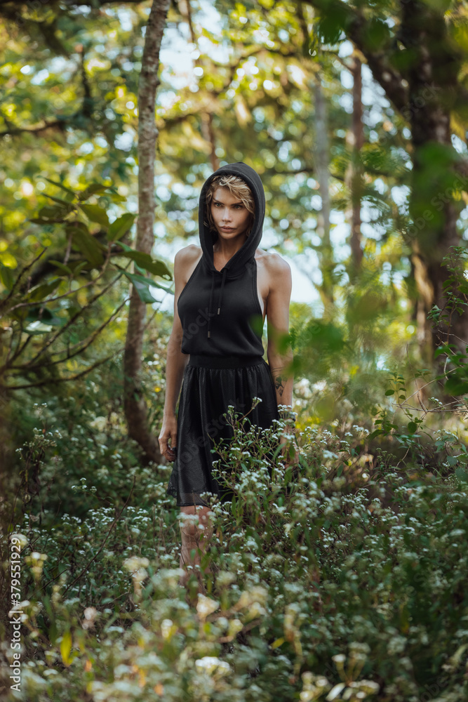 Brooding dreamy young girl blonde, black dress with a hood standing by a tree. The girl got lost in the woods. Trekking, fantasy, magical mystical forest. Girl standing by a tree. High quality photo Brooding dreamy young girl blonde, black dress with a hood standing by a tree. The girl got lost in the woods. Trekking, fantasy, magical mystical forest. Girl standing by a tree. High quality photo