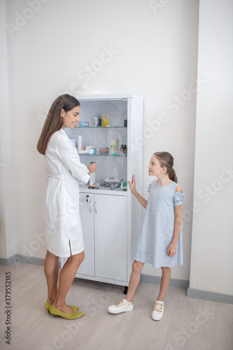 Little patient talking to the doctor near the vitrine with medicines