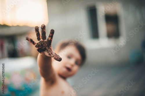 Caucasian undressed boy with dirty hand is playing outside in the ground having fun in a summer day