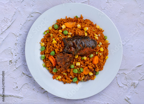 Jollof Rice and vegetables with stewed Goat meat in a white ceramic plate on an embossed background