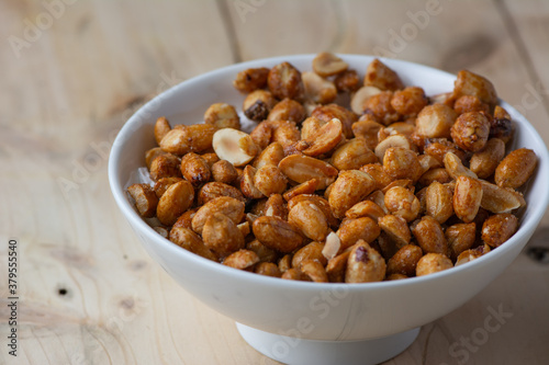 Honey coated Groundnuts / Peanuts in a while ceramic bowl on a wooden background