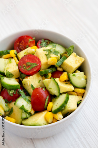 Fresh Avocado Tomato Salad in a bowl on a white wooden background, side view.