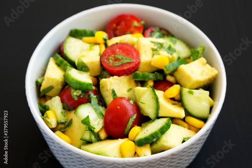 Fresh Avocado Tomato Salad in a bowl on a black surface, side view. Close-up.