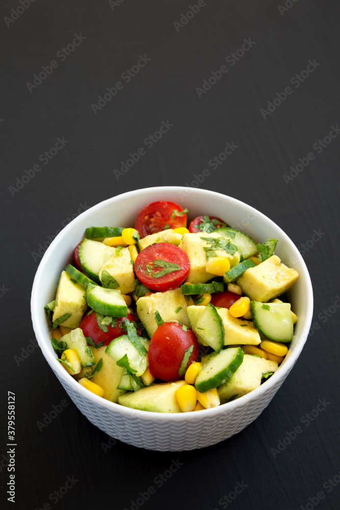 Fresh Avocado Tomato Salad in a bowl on a black background, top view. Flat lay, overhead, from above. Copy space.