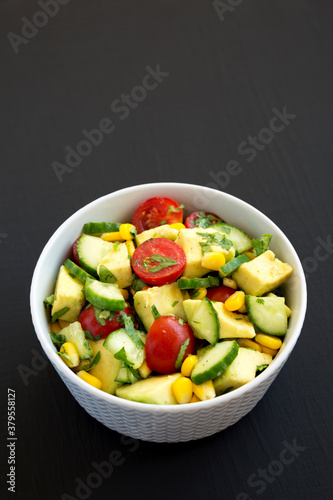 Fresh Avocado Tomato Salad in a bowl on a black background, top view. Flat lay, overhead, from above. Copy space.