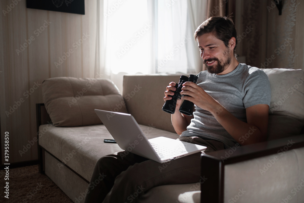 Funny man looking searching binoculars a laptop on the table working at home office. Funny man looking searching binoculars a laptop on the table working at home office.
