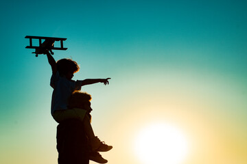 Sunset silhouette of Father carrying his son on shoulders. Child son pilot and dad daddy father with airplane.