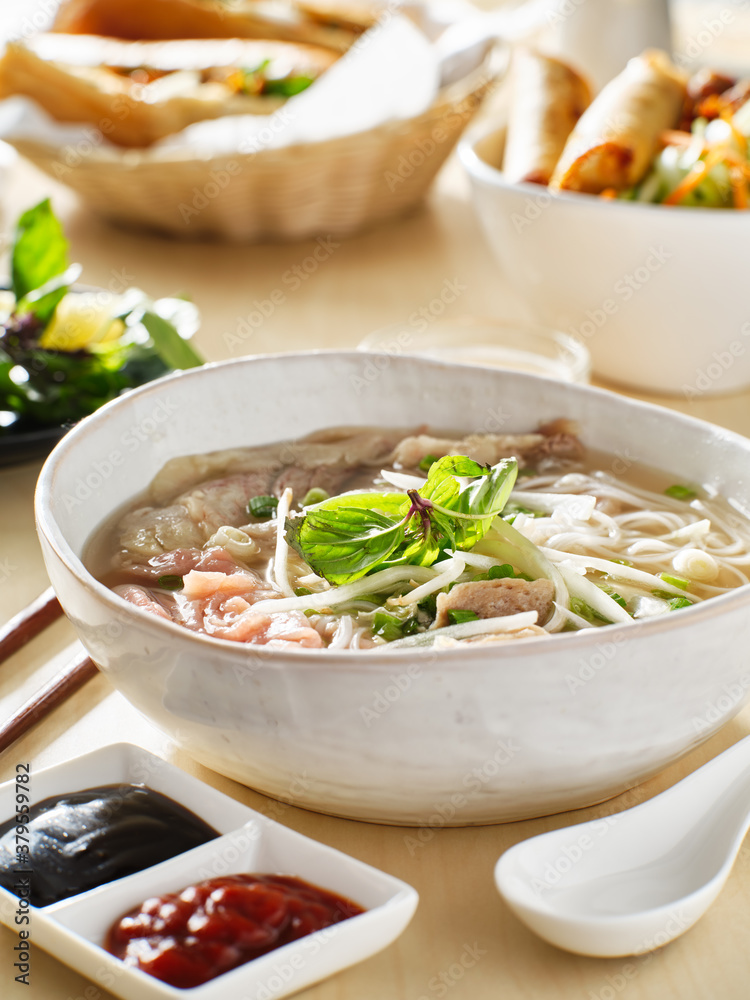 vietnamamese meal with beef pho bo soup accompanied by hoisin sauce and sriracha