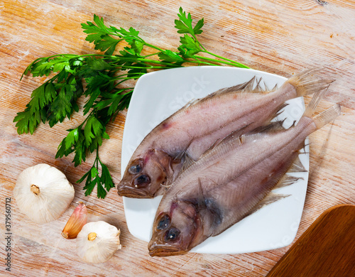 Uncooked roosterfish with greens and garlic on wooden board before cooking photo