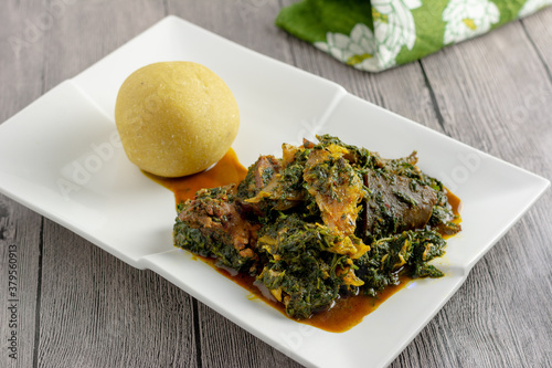 Afang soup served with eba on a white ceramic plate, wooden background photo