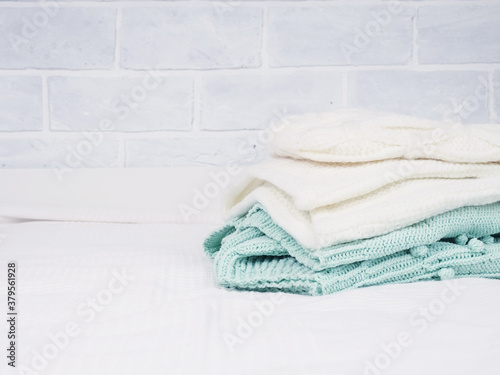 A stack of warm knitted things on a white bed. Cozy clothes. Household concept. folded knitted things white